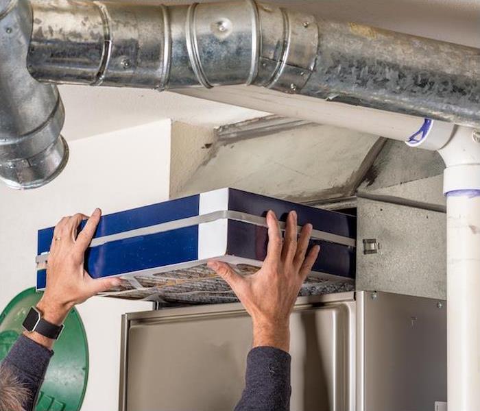 a person in a blue shirt reaching up to change a furnace filter
